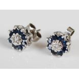 A pair of white metal sapphire and diamond set cluster earrings, circa 1970, each centred with a