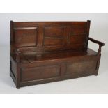 A 18th century oak settle, the rectangular triple panelled back above a planked seat with hinged