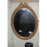 A SMALL OVAL GILT FRAMED WALL MIRROR WITH RIBBON TIED SURMOUNT 600.