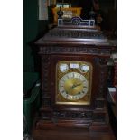 AN EARLY 20TH CENTURY CARVED MAHOGANY TABLE CLOCK WITH BRASS DIAL, TWO TRAIN MOVEMENT CHIMING ON TWO