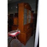 A VICTORIAN BLONDE OAK TWO PART BOOKCASE, THE UPPER SECTION WITH BROKEN PEDIMENT CENTRED BY A