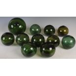 A group of eleven green glass fishing floats, comprising one approximately 20cm, and ten