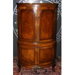 An early 20th Century walnut corner cocktail cabinet, the upper cupboard doors opening to a mirrored