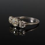 A white metal three stone diamond ring, centred with an old cushion cut diamond calculated to