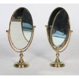 Pair of brass table/ dressing table mirrors, of oval form with swing plates on round plinth bases,