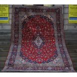A Persian Kashan rug, the deep red field with floral and leafy vine around a double indigo and ivory