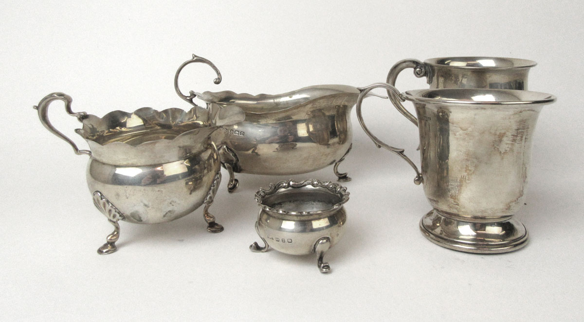 An assortment of silver items to include two mugs, a sauce boat, a cream jug and a salt.