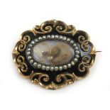 A late Georgian yellow metal and black enamel mourning brooch having a hair work panel surrounded