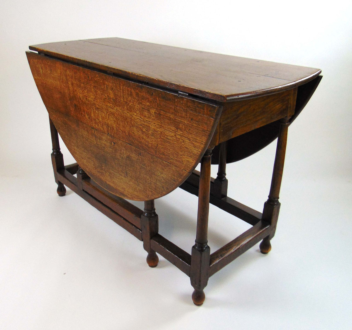 An 18th century oak drop leaf table, the oval top supported on a single gate action on turned legs,