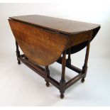 An 18th century oak drop leaf table, the oval top supported on a single gate action on turned legs,