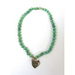 A continuous pale green jade bead necklace suspending a 9ct yellow gold heart shaped locket, bead d.