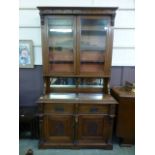 An early 20th century oak dresser having a raised glazed two door bookcase above two drawers above