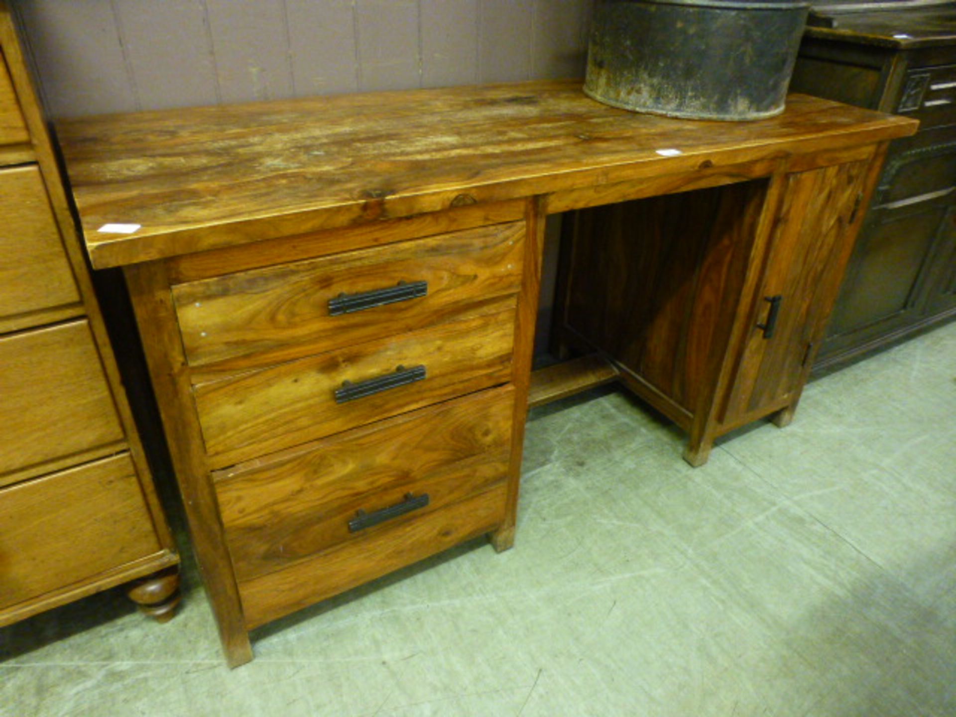 An Indonesian hardwood desk having a bank of three drawers with cupboard door