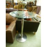 A circular glass topped table on chromed base