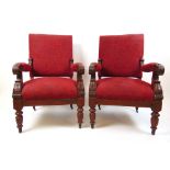 A pair of Victorian walnut open arm chairs upholstered in a floral patterned red fabric,