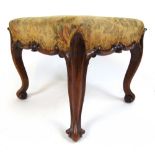 A Victorian walnut foot stool upholstered in a floral needlework fabric on carved and moulded