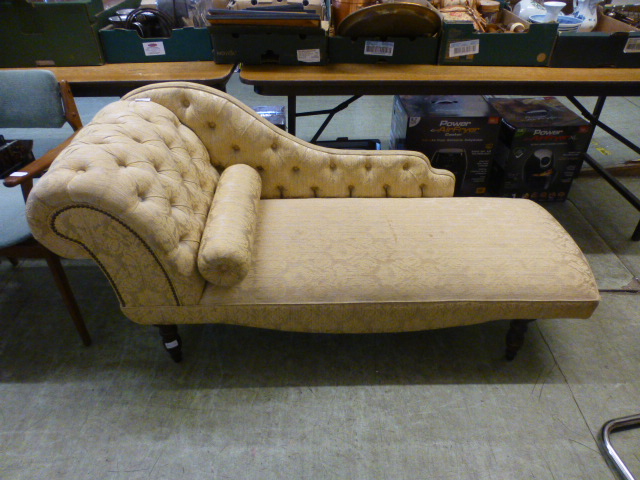 A chaise lounge upholstered in a button back patterned gold fabric