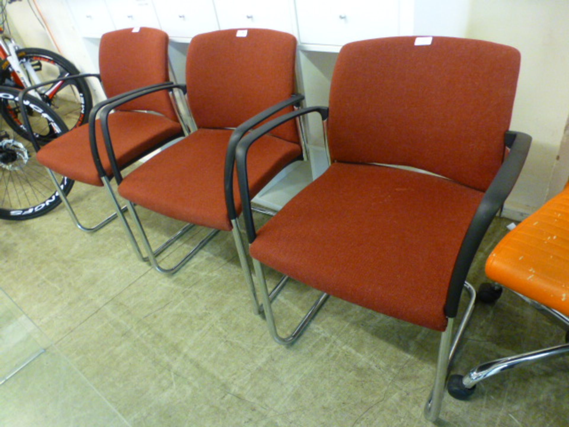 A set of three office arm chairs upholstered in a wine fabric on chrome base