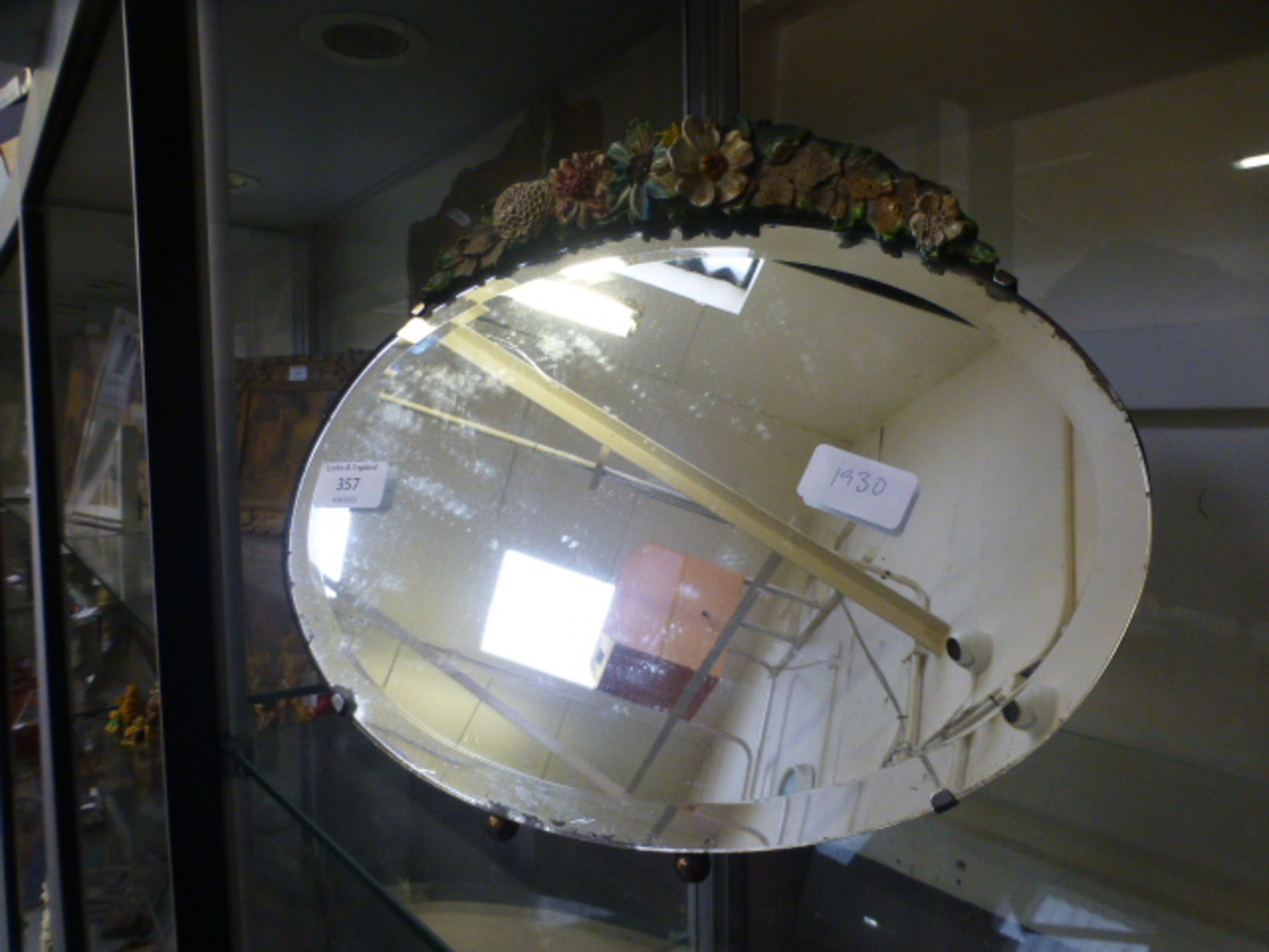 A mid-20th century oval easel mirror with floral decoration to top