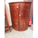 An 18th century mahogany inlaid bow front wall hanging corner cupboard with two doors enclosing