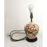 A Moorcroft lamp base with decorated in a purple, yellow and green floral pattern on a cream ground,