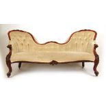 A Victorian walnut arch back settee upholstered in a beige button back cut fabric on cabriole legs,