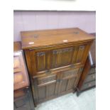 A mid-20th century oak drinks cabinet having a pull down linen fold design flap to top with two