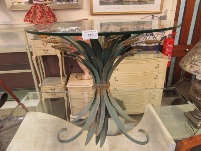 A circular glass topped table with a green metal leaf base