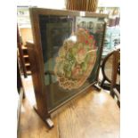 An early twentieth century oak fire screen/ occasional table with floral needle work panel