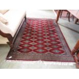 A modern hand-woven Indian rug border surrounding red ground field with geometric octagons