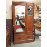 An arts and crafts oak wardrobe with beveled mirror door flanking leaded glass over single drawer
