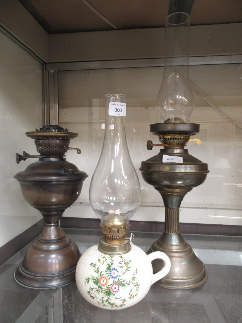 Two early 20th century brass effect oil lamps together with a ceramic oil lamp with glass funnel