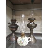 Two early 20th century brass effect oil lamps together with a ceramic oil lamp with glass funnel