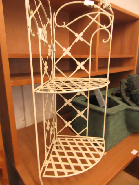 A cream painted white metal corner shelf unit