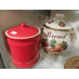 A large ceramic bread bin with fruit design together with a red and white ceramic bread bin