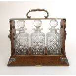 An early 20th century oak and silver plate mounted tantalus with three hobnail cut glass decanters.