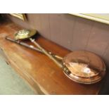 A copper bed warming pan together with a modern brass embossed bed warming pan