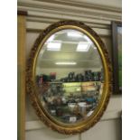 An ornate gilt framed oval bevel glass wall mirror