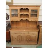A waxed pine dresser having a raised top section with a pair of glazed doors and four small drawers,