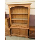 A waxed pine full height cabinet having a raised bookcase to the top with three small drawers on a