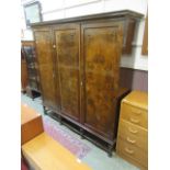 An early 20th century burr walnut three door wardrobe on turned legs and stretchers