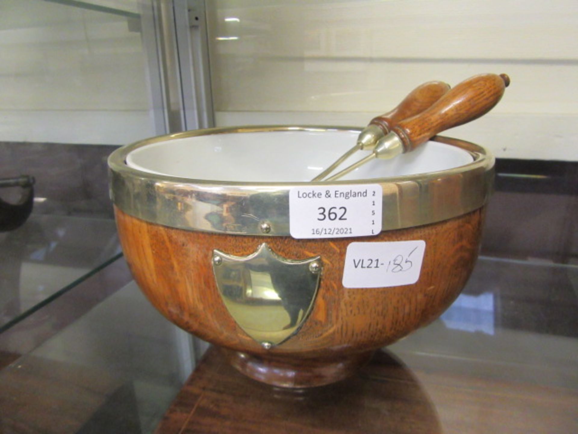 A plated rimmed oak salad bowl with white ceramic liner and utensils