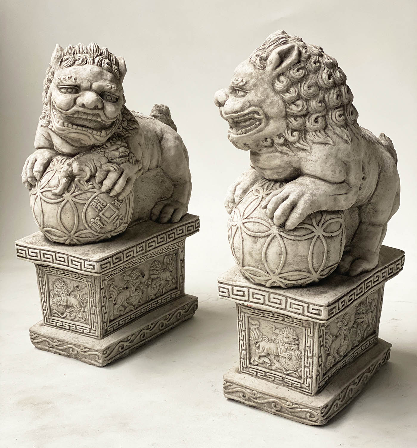 GARDEN DOGS OF FOO, an opposing pair, weathered, reconstituted stone with Greek key and lion