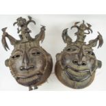 BENIN TRIBAL MASKS, a pair, bronze, cast patterned faces with seated figure surmount and stylised
