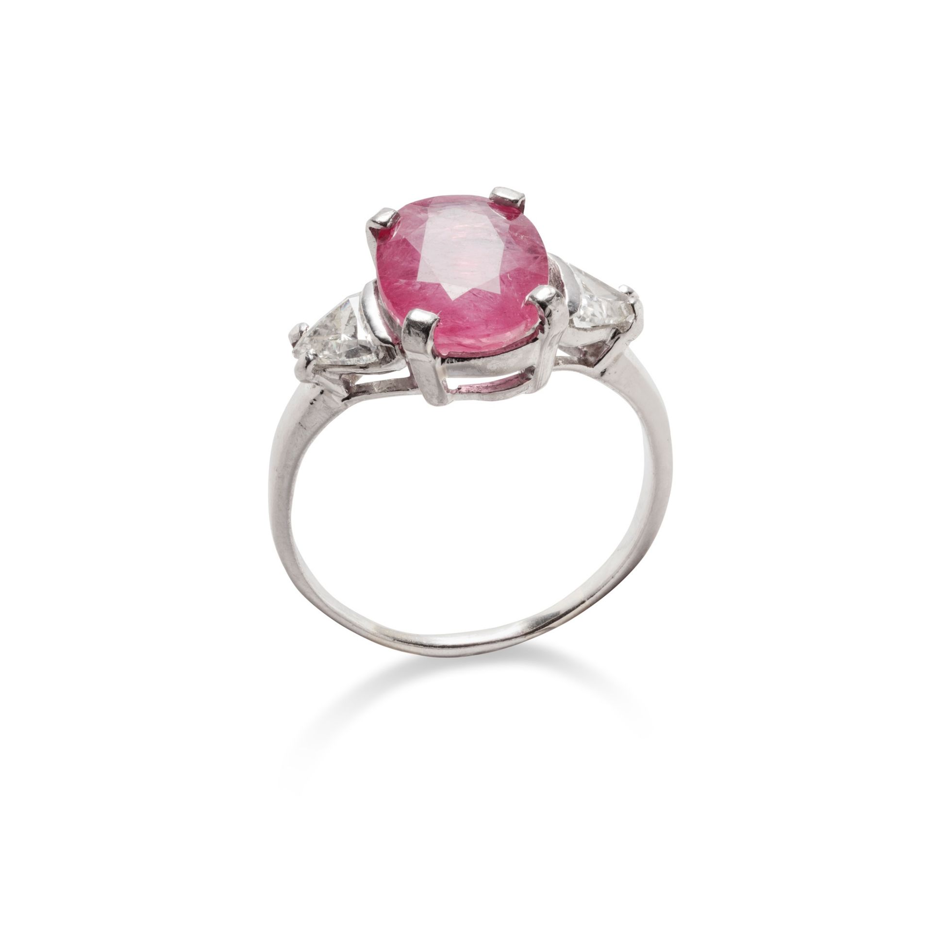 A ruby and diamond ring The oval-cut ruby in a four-claw mount, between triangular-cut diamond