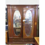 An Edwardian inlaid mahogany two door wardrobe, the doors with oval bevelled mirrors, above two