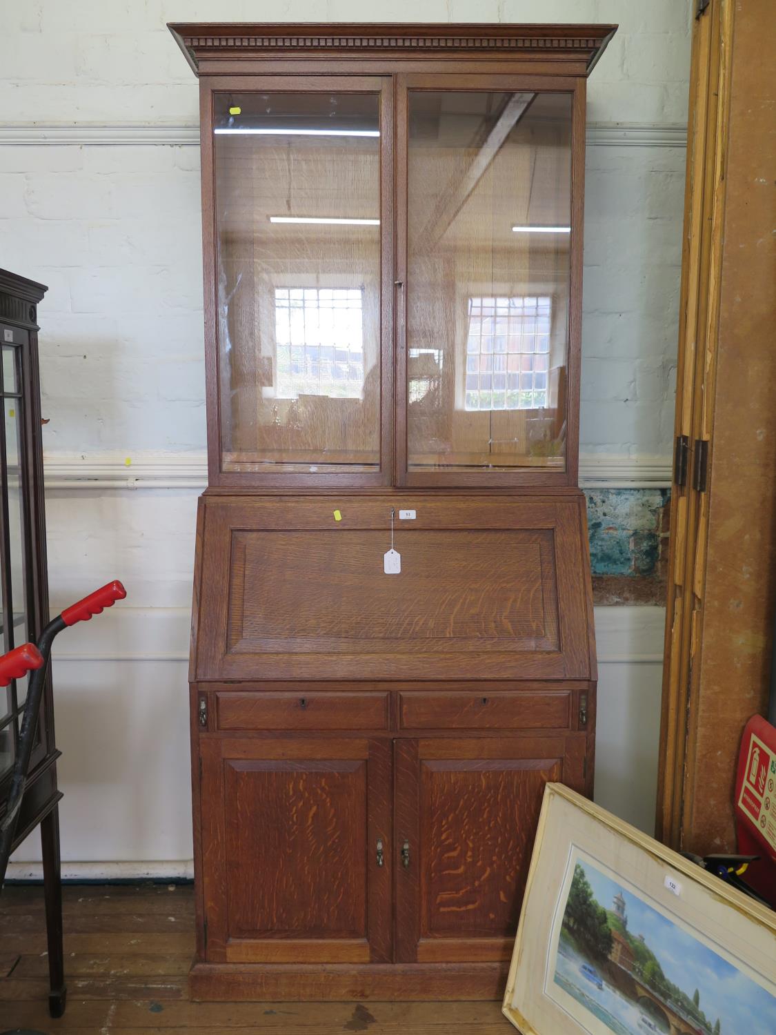 An oak bureau bookcase, the twin glazed doors over a sloping fall enclosing a fitted interior over