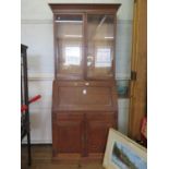 An oak bureau bookcase, the twin glazed doors over a sloping fall enclosing a fitted interior over