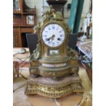 A French gilt metal and porcelain mounted mantel clock, deipicting musical instruments, armour and
