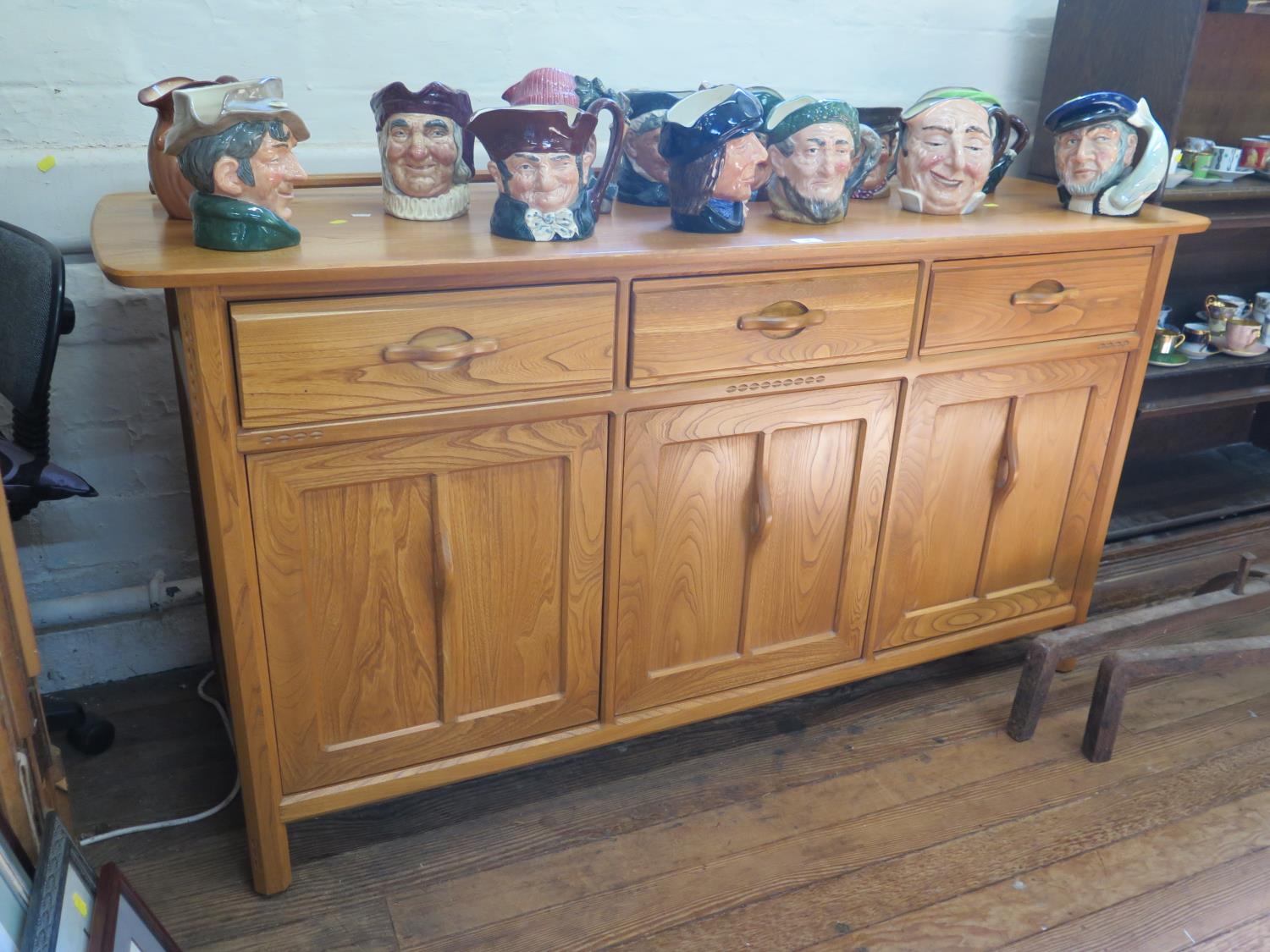 A light elm Ercol sideboard, with three frieze drawers over three panelled cupboard doors, on